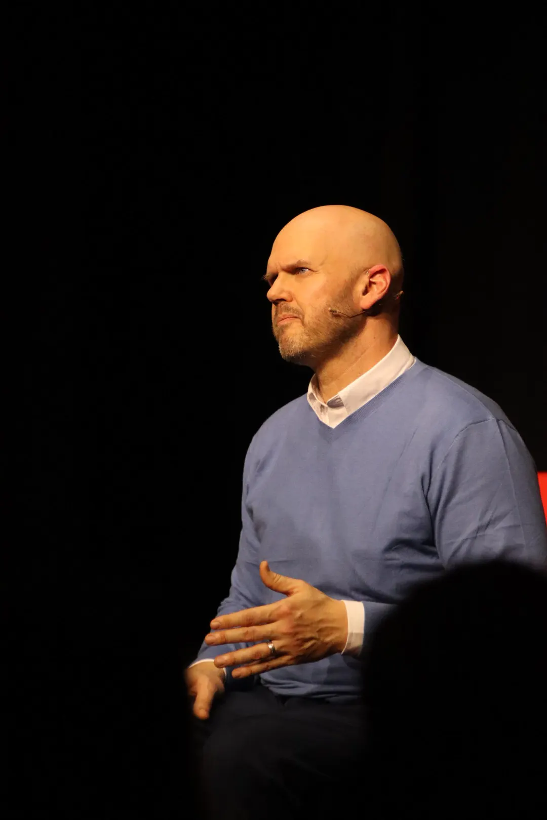 Jeff D. Harmon seated on stage under a spotlight, mid-talk
