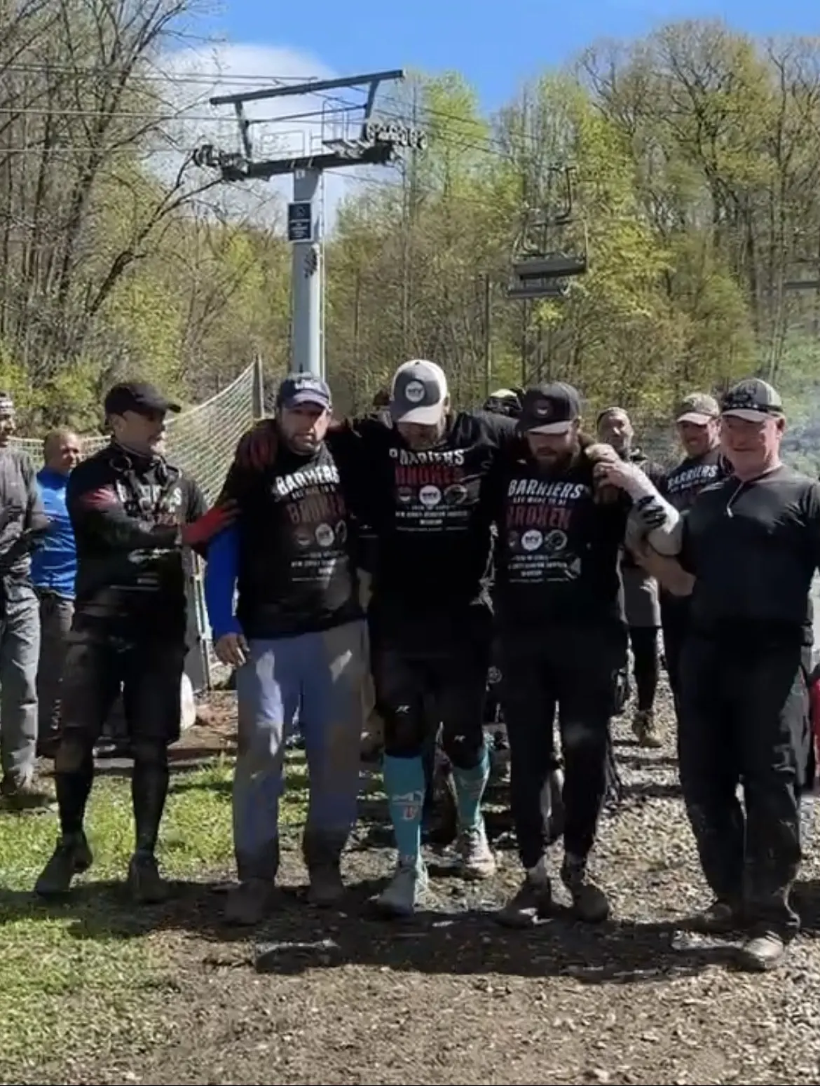 A team standing arm in arm in Barriers Are Made To Be Broken shirts at the bottom of a mountain trail