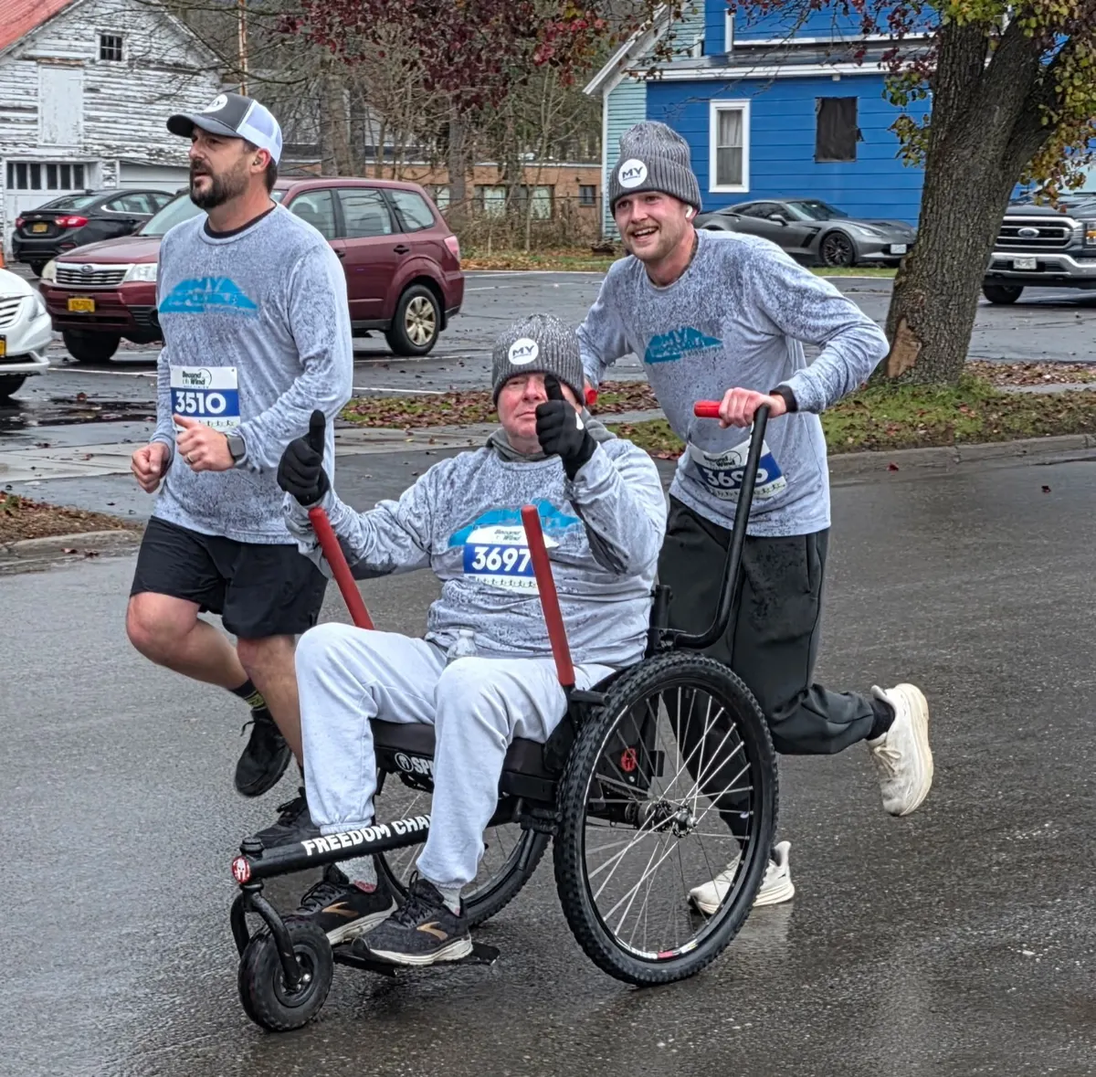 Two runners pushing a rider in a Freedom Chair through a rainy race course